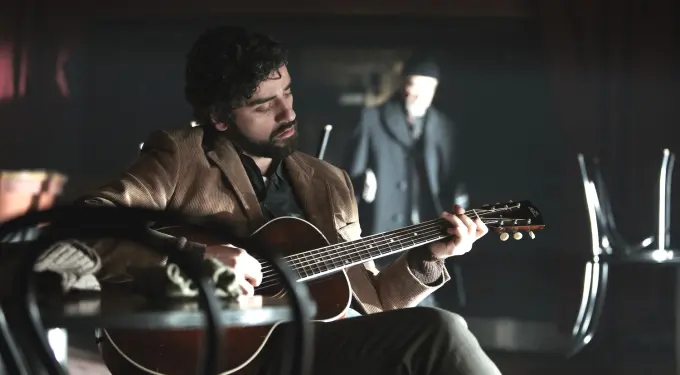 Oscar Isaac playing guitar in dimly lit Interior scene from Inside Llewyn Davis
