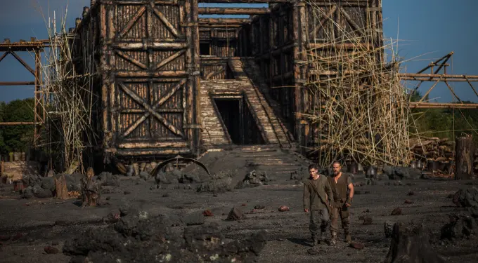 two men walk past a large wooden structure under construction