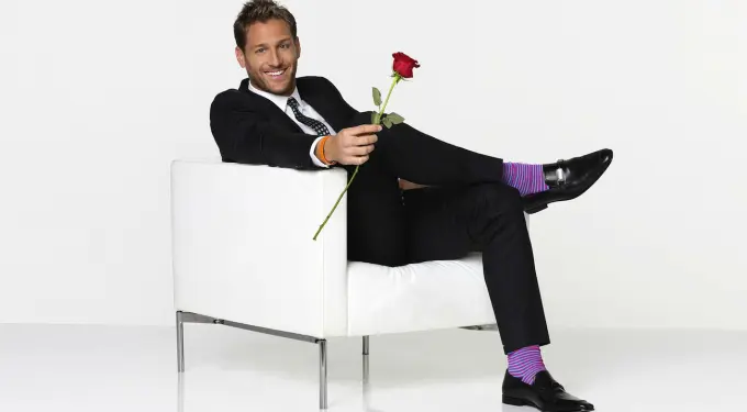 Juan Pablo Galavis in suit holding rose seated on white chair