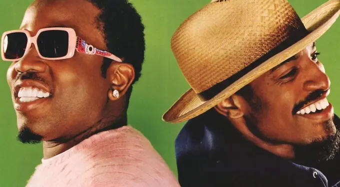 Two smiling men back-to-back, one wearing pink sunglasses, the other a straw hat