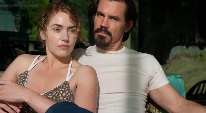 Man and woman sitting closely on a bench outside, serious expressions