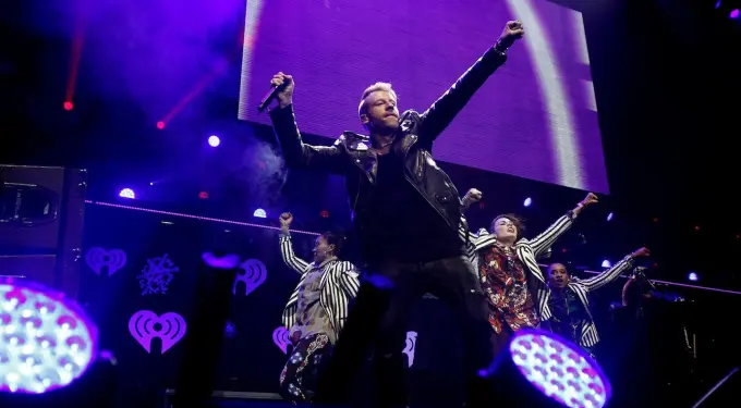 Macklemore raises fists holding microphone on stage with backup dancers