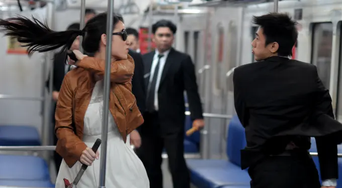 Woman in brown jacket attacks man in black suit with hammer