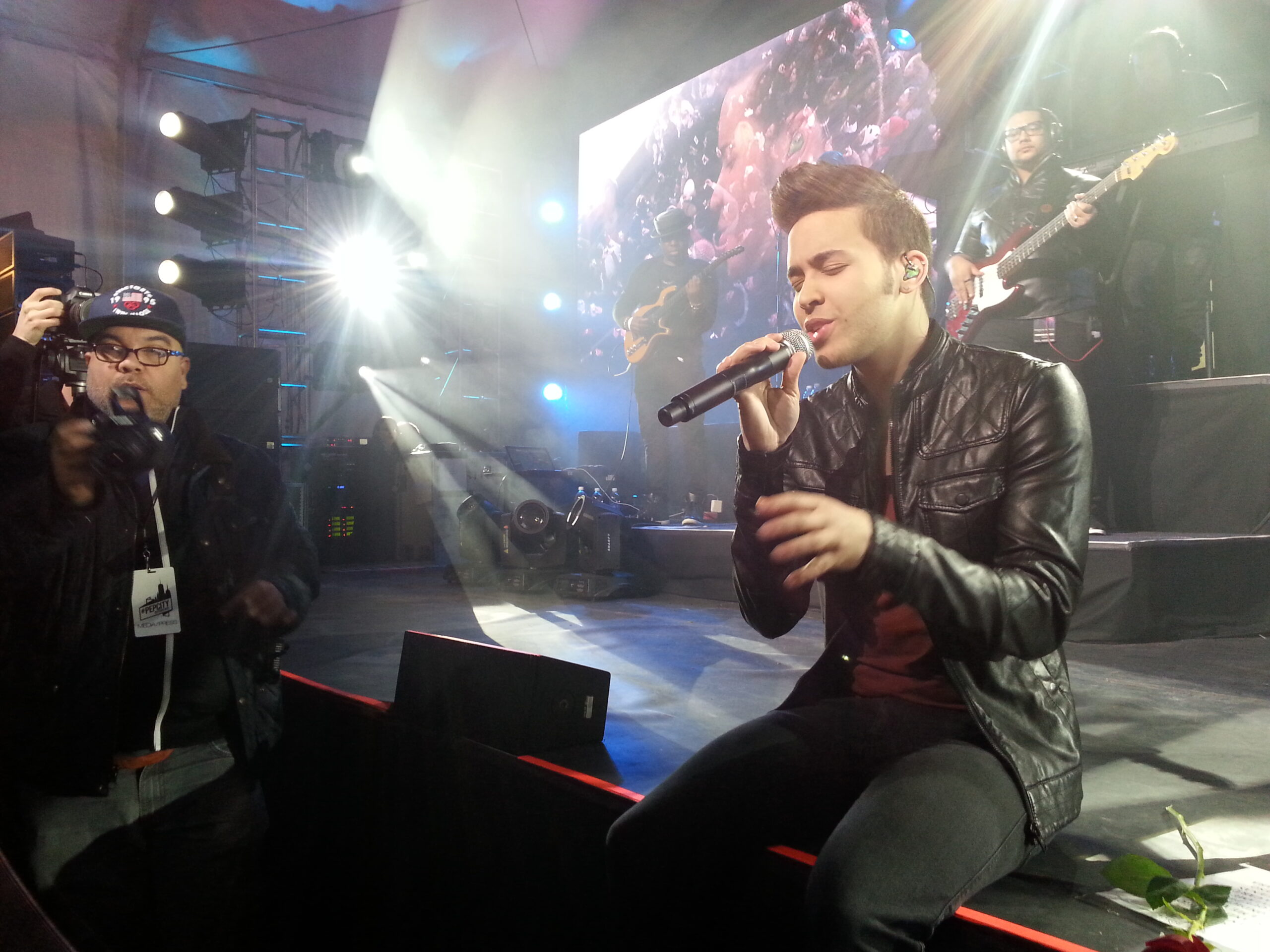 Prince Royce singing live on stage holding microphone with band behind