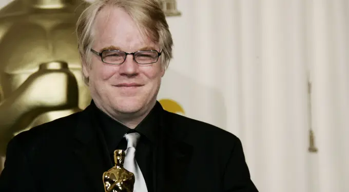 Philip Seymour Hoffman holding Oscar statuette, smiling in black suit