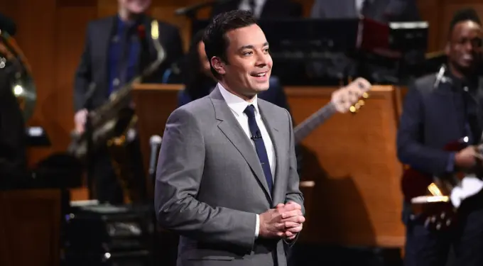 Jimmy Fallon speaking on stage with band behind him
