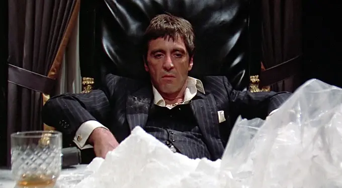 Al Pacino as Tony Montana sits at desk with cocaine pile