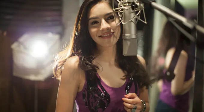 Cáthia smiles close to a microphone in a recording studio