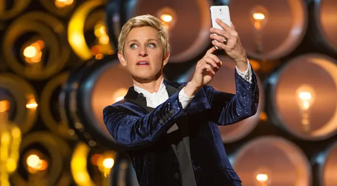 Ellen DeGeneres in tuxedo taking a selfie during the Oscars