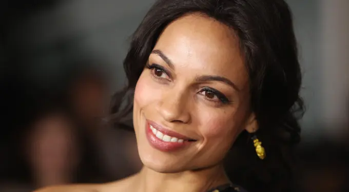Close-up headshot of Rosario Dawson smiling with earrings