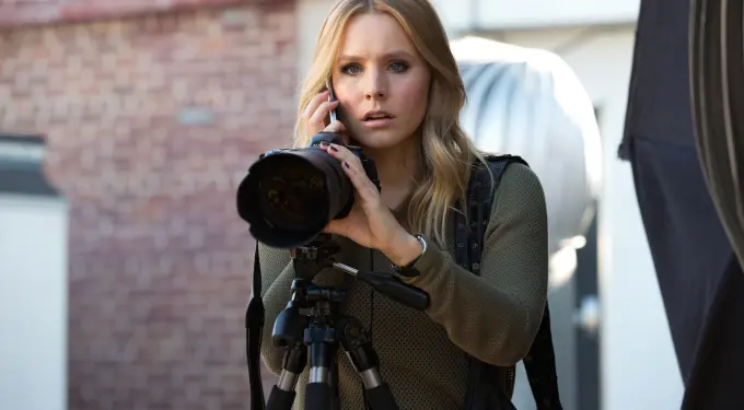 Kristen Bell holding camera and phone with focused expression