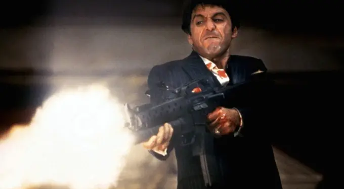 Tony Montana character firing a large gun with grimace in scene