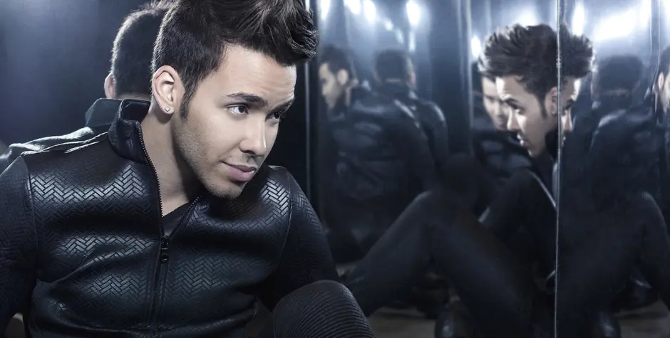 Prince Royce photographed for a 2014 promotional shoot.
Prince Royce in black jacket sitting against mirrored walls