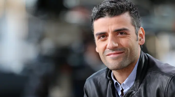 Oscar Isaac smiling in a leather jacket during Cannes interview