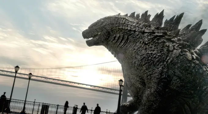 Godzilla towering by bridge with people silhouetted below at sunset