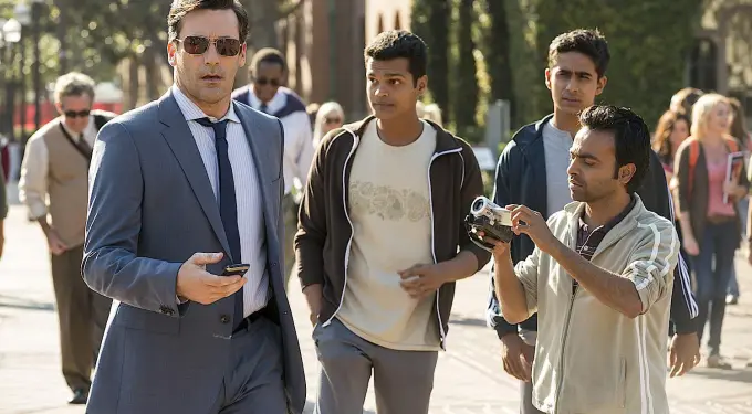 man in suit with phone walks while another films with a video camera