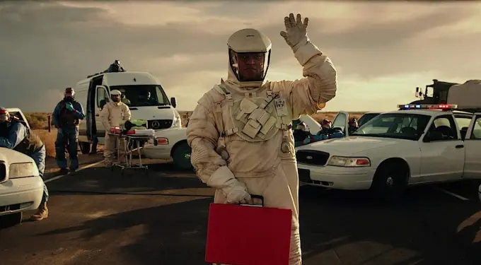 Laurence Fishburne in protective spacesuit waving on road with police cars