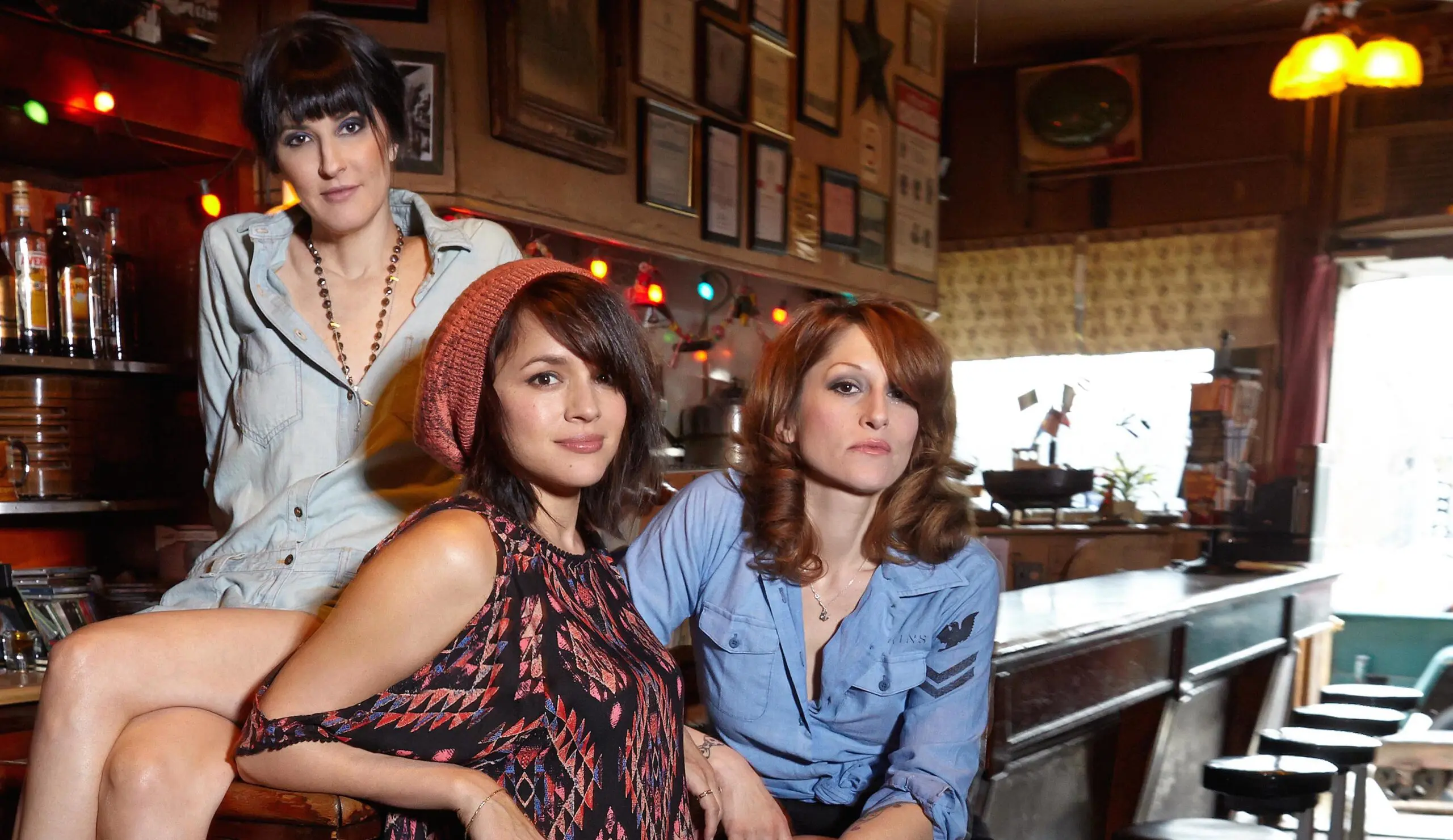 Three women posing in a bar with colorful string lights and framed pictures