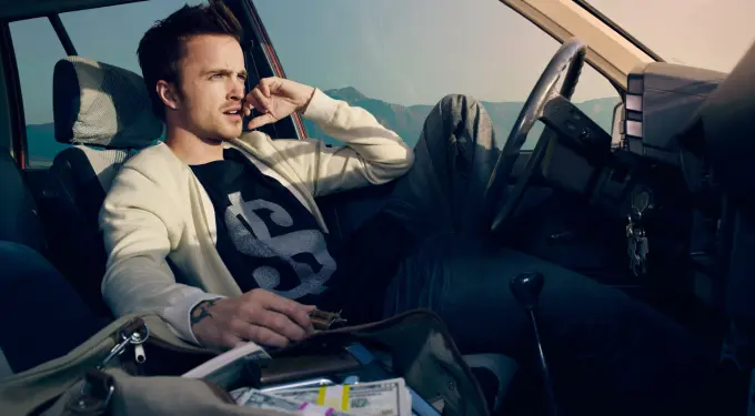 Aaron Paul sitting in car, looking outside, holding an object