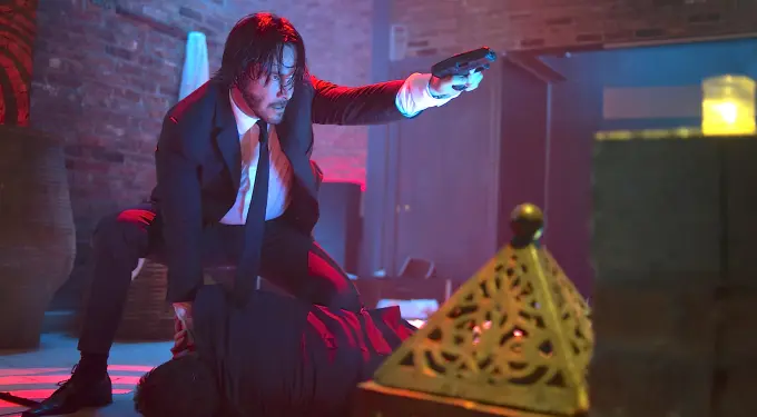 Keanu Reeves holding gun and pinning man to floor in action scene