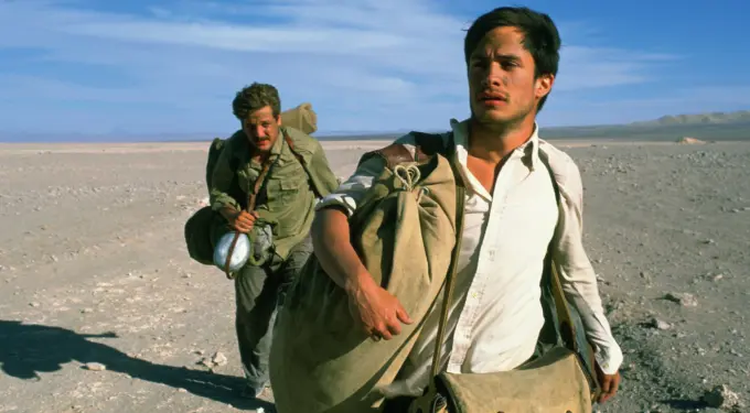 two men hiking through desert carrying heavy bags