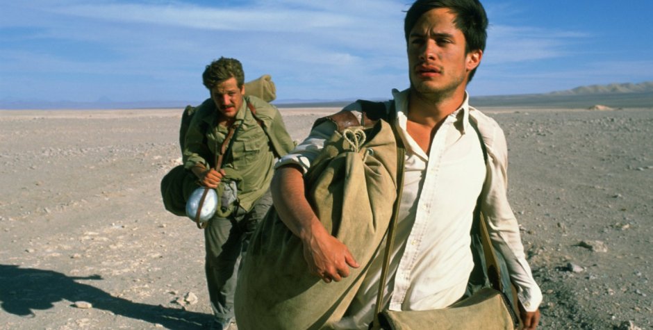 two men hiking through desert carrying heavy bags