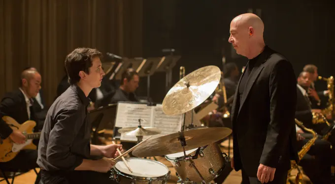 Young drummer sitting at drum set, staring at intense bald instructor