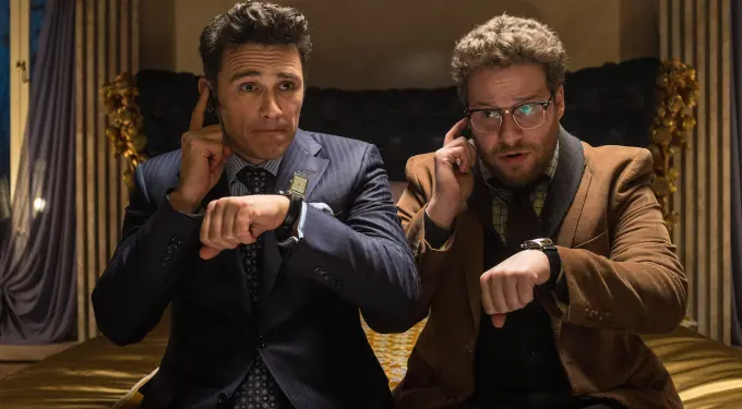 Two men in suits check watches and earpieces while sitting on bed