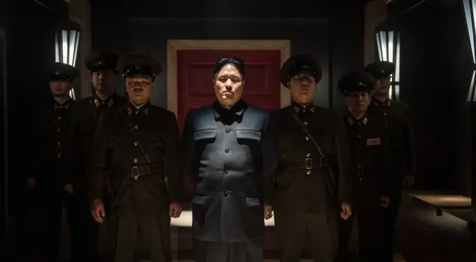 Randall Park stands in dark room with six military men behind him