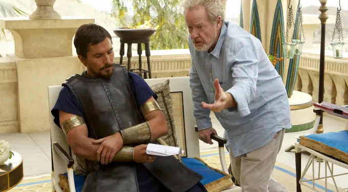 Christian Bale in armor seated, Ridley Scott directing on set