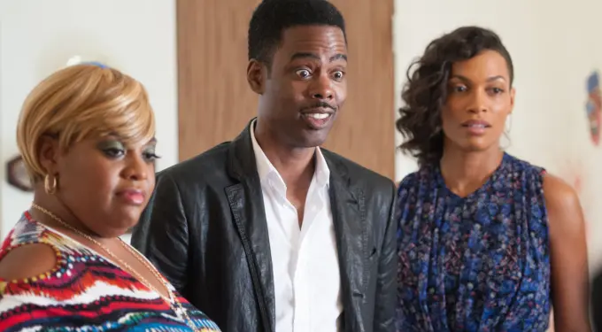 Chris Rock in leather jacket with two women in colorful outfits indoors