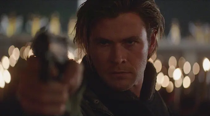 Chris Hemsworth aiming a gun with a serious face in nighttime scene