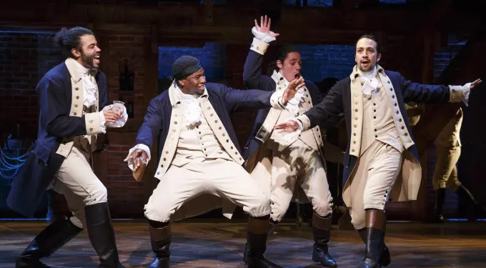 Four male actors in Hamilton costumes sing and dance on stage