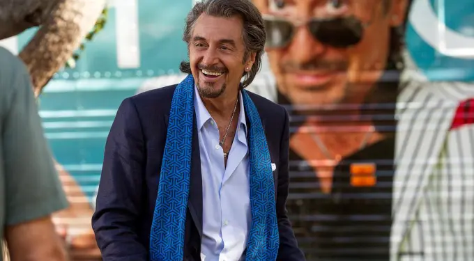 Al Pacino smiling wearing blue scarf and dark jacket outdoors
