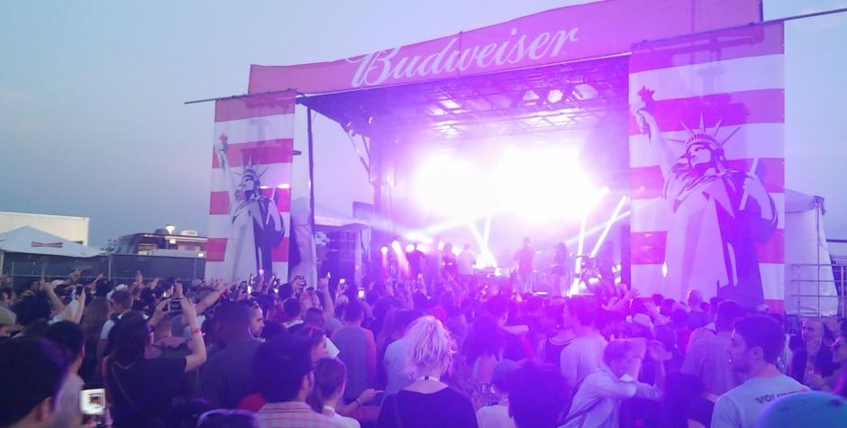 Crowd gathers at Budweiser-sponsored concert stage with purple lighting at dusk.
Outdoor Budweiser concert stage with crowd and bright purple lights