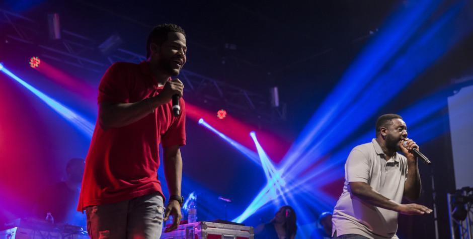 Two male performers sing with microphones on stage under blue and red lights