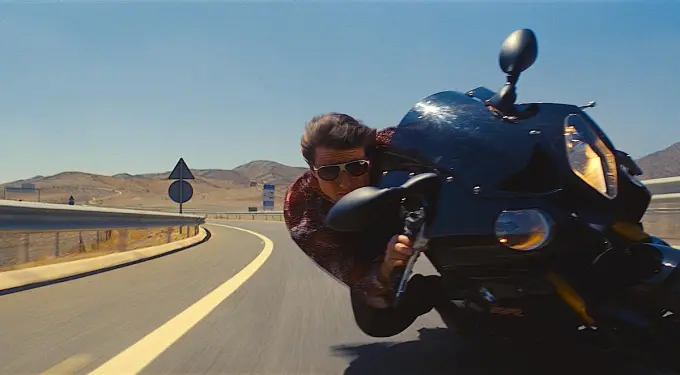 Tom Cruise leaning on motorcycle during a high-speed chase scene