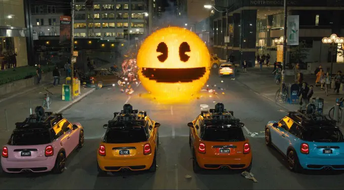 Four mini cars face giant pixelated Pac-Man on city street at night