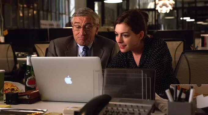Older man and younger woman focused on laptop in office setting