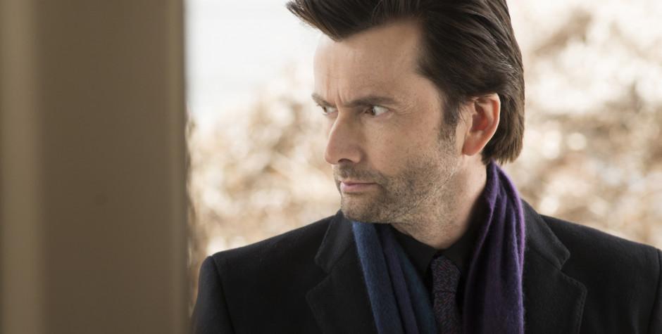 David Tennant looking sideways in dark coat and scarf, serious expression
