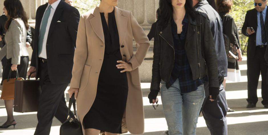 Two women in coats walk near courthouse columns in daylight