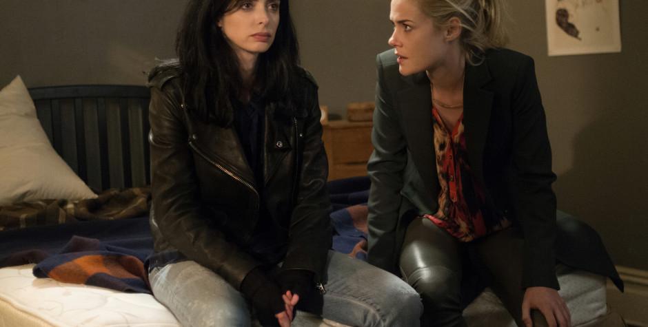 two women seated on a bed having a serious conversation indoors
