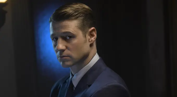 Ben McKenzie in dark suit looks sideways in moody headshot