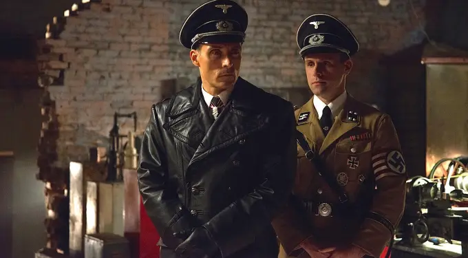 two men in Nazi uniforms inside a dimly lit industrial setting