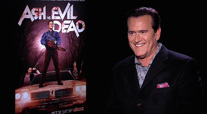 Bruce Campbell smiles in interview with Ash vs Evil Dead poster behind him