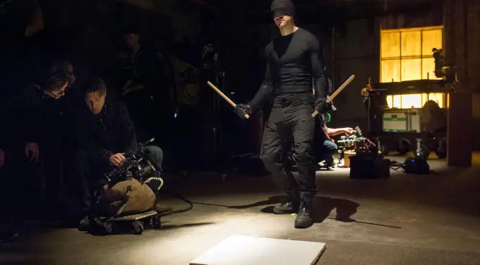 Blindfolded man in black holds sticks on Daredevil set with crew
