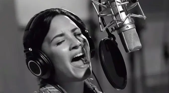 Demi Lovato singing into studio microphone with headphones, eyes closed