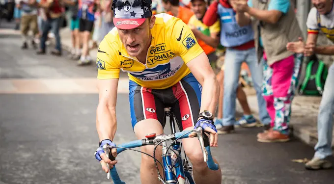 Ben Foster cycling aggressively in yellow jersey with spectators clapping