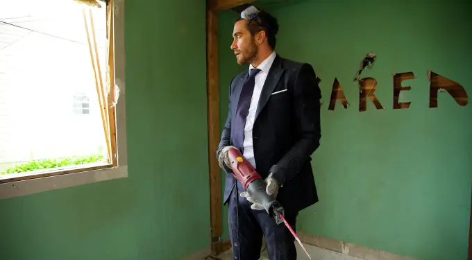 man in suit holding power saw in damaged room with torn green walls