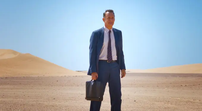 Tom Hanks in a suit holding a bag in the desert